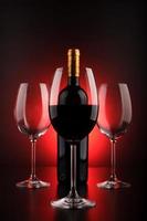 Botellas de vino y vaso lleno con fondo rojo y negro. foto