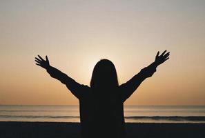 Woman's silhouette with arms open at the beach photo