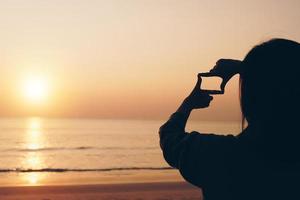 Selective focus of woman's hands making frame with sunrise photo