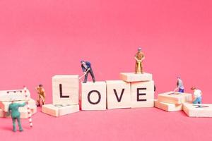 Trabajadores en miniatura construyendo la palabra amor en bloques de madera con un fondo rosa, concepto del día de San Valentín foto