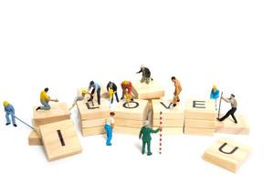 Miniature workers building the word Love on wooden blocks with a white background, Valentine's Day concept photo