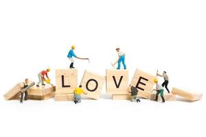 Miniature workers building the word Love on wooden blocks with a white background, Valentine's Day concept photo