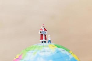 Miniature Santa Claus holding gifts for kids on a globe, Merry Christmas concept photo