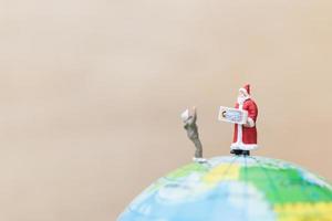 Miniature Santa Claus holding gifts for kids on a globe, Merry Christmas concept photo