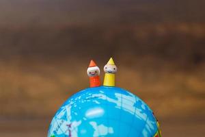 Miniature wooden dolls on a globe with a wooden background photo