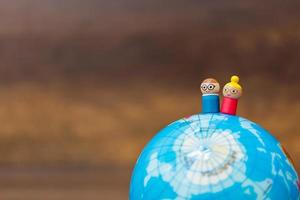 Miniature wooden dolls on a globe with a wooden background photo