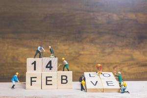 Miniature workers building the words and dates for Valentine's Day on wooden blocks with wooden background, Valentine's Day concept photo