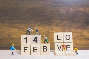 Miniature workers building the words and dates for Valentine's Day on wooden blocks with wooden background, Valentine's Day concept photo