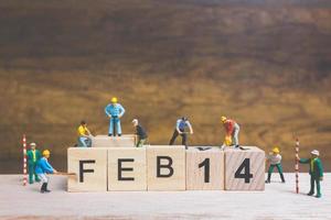 Trabajadores en miniatura construyendo las palabras y fechas para el día de San Valentín en bloques de madera con fondo de madera, concepto del día de San Valentín