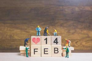 Trabajadores en miniatura construyendo las palabras y fechas para el día de San Valentín en bloques de madera con fondo de madera, concepto del día de San Valentín