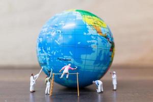 Miniature painters painting on a globe with a wooden background, save the Earth concept