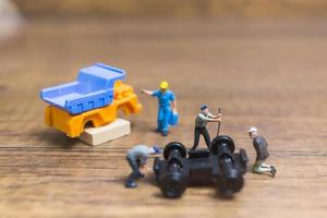 Miniature workers repairing a wheel off a truck on a wooden background photo