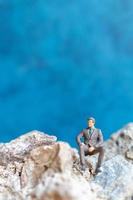 Miniature businessman sitting on a rock with a blue background photo