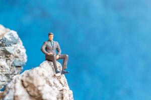 Miniature businessman sitting on a rock with a blue background photo