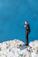 Miniature businessman standing on a rock with a blue background photo