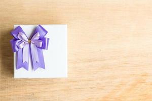 Purple ribbon bow on a white gift box on a wooden background photo