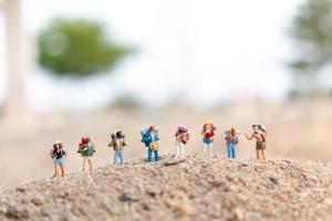 Viajeros en miniatura con mochilas caminando sobre arena, concepto de viaje y aventura