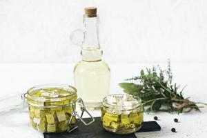 Feta marinado en un frasco de vidrio, especias y aceite de oliva aromatizado sobre un fondo de madera foto