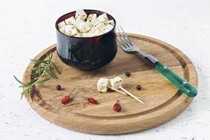 Feta marinado en un plato sobre una tabla de madera con especias sobre un fondo blanco. foto