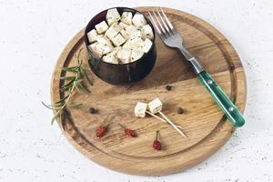 Feta marinado en un plato sobre una tabla de madera con especias sobre un fondo blanco. foto