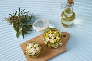 Marinated feta in a glass jar and spices against a blue background photo