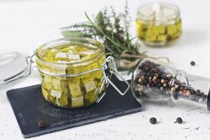 Marinated feta in a glass jar and spices against a white background photo