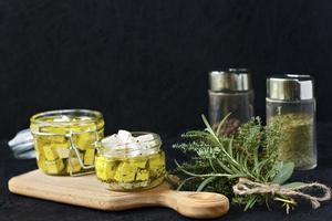 Marinated feta in a glass jar and spices on a black background photo