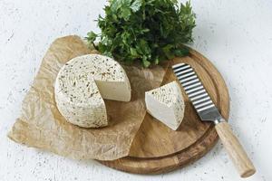 White cheese on a wooden board on a white background with greens photo