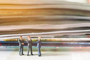 Miniature businessmen standing with a stack of books with warm lighting background photo