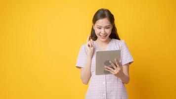 Asian woman smiling and looking at tablet on yellow background photo