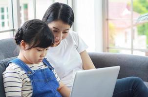 Asian mother happily sits teaching her daughter reading homework photo