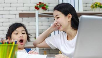 madre asiática felizmente se sienta enseñando a su hija a leer la tarea foto