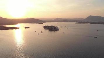 Lake Pichola golden view during sunset with Taj Lake Palace in the center, in Udaipur, Rajasthan, India - Aerial wide Orbit shot video