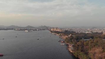 Wide Panoramic view of Pichola lake bank with Taj lake palace in the distance at sunset, in Udaipur, Rajasthan, India-  Aerial high Panoramic shot