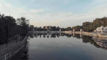 Shore view of lake Pichola Ascending to Ambrai Ghat and revealing the surrounding Old town, in Udaipur, Rajasthan, India - Aerial ascending Fly-over reveal shot video