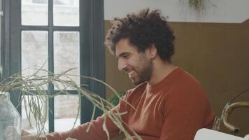 Laptop on table in front of young Middle Eastern man, tilt up, head of man, eyes on laptop, laughs, tilt down, hands on laptop, vase in front on the left video