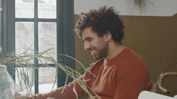 Young Middle Eastern man sits at table watching laptop in front of him, laughs video