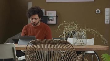 giovane uomo mediorientale si siede al tavolo, digitando sul computer portatile