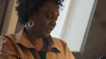 Close up of hands of mature black woman at table, typing on laptop and holding phone whilst talking video