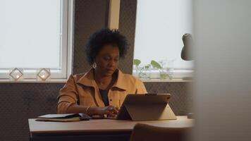 Mature black woman sits at table, having video call