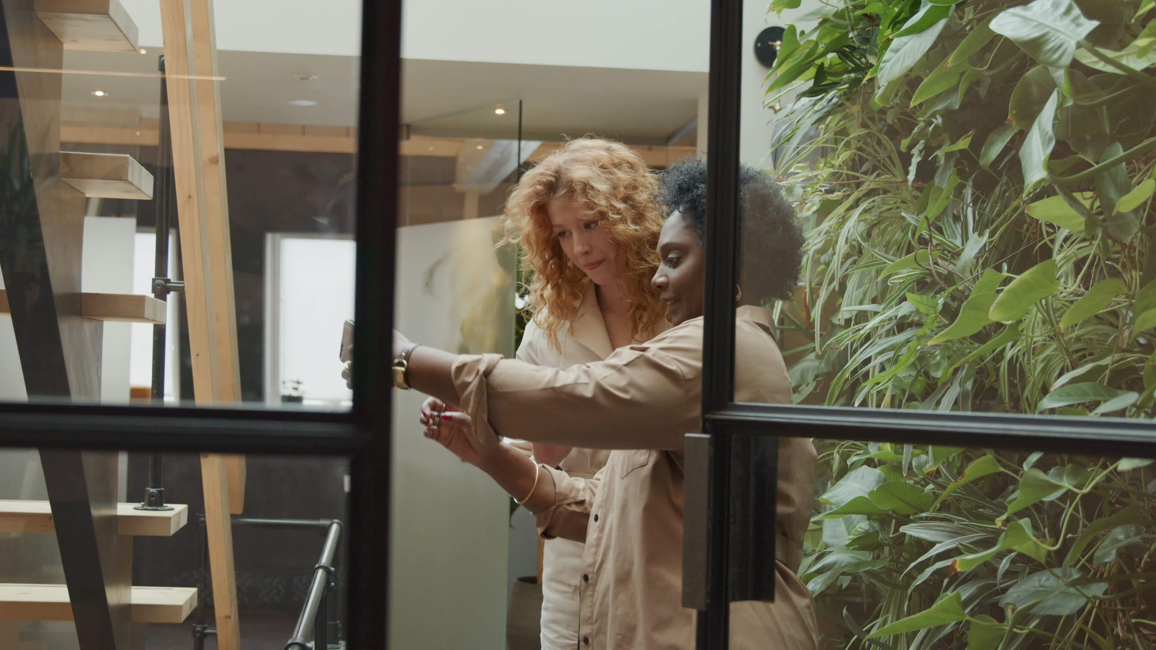 Black mature woman and young white woman standing in hallway, black woman makes photo of them with mobile phone, smiling