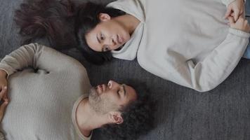 Young mixed race woman and young Middle Eastern man lying on their back on floor, in opposite direction, head touching shoulder, talking video