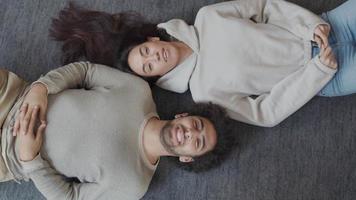 giovane donna di razza mista e giovane uomo mediorientale sdraiato sulla schiena sul pavimento, in direzione opposta, la testa che tocca la spalla, ridendo