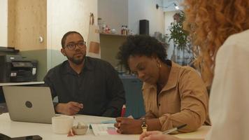 mujer madura negra, mujer joven blanca y hombre negro con gafas, sentado a la mesa, tener una reunión en la oficina