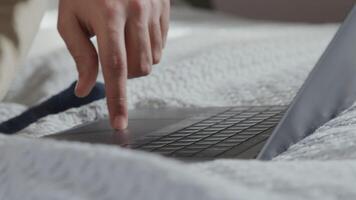 Gros plan d'un ordinateur portable sur le lit et les mains d'un jeune homme du Moyen-Orient, défilement sur le pavé tactile et clavier de saisie video