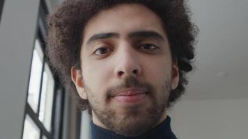 Close up and slow motion of young Middle Eastern man, looking into camera lens, bottom up shot, eyes following camera, smiling a bit video