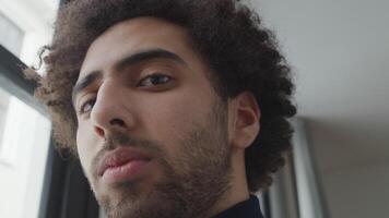 Close up of young Middle Eastern man, head slightly turned down, looking seriously into camera lens, eyes following video