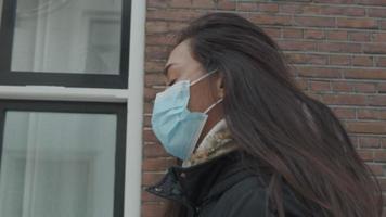 hoofd geschoten van jonge gemengd ras vrouw met gezichtsmasker op, wandelingen in straat langs huizen