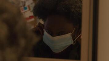 Close up of mirror with black mature woman, putting on face mask, with both hands, adjusting it, whilst looking into mirror, turns, walking down the stairs in hallway, looks into mirror, leaves video