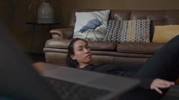 jonge vrouw van gemengd ras liggend op de vloer, sit-up oefening, terwijl het kijken naar laptop naast haar video